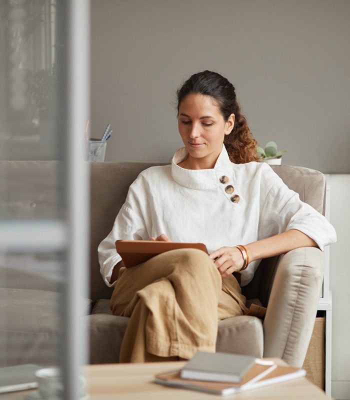 Portrait of modern successful businesswoman using digital tablet while relaxing on couch in office, copy space